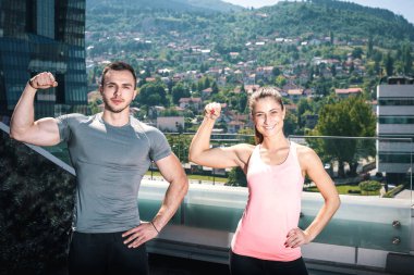 İki genç yetişkin fitness model kentsel sahne binasının çatı üzerinde açık poz. Kaslı fit vücut gösterilen.