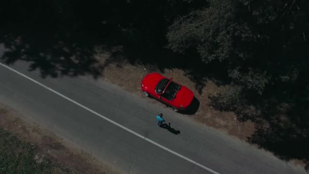 Mladý muž kráčí lesem a nastupuje do červeného auta. — Stock video