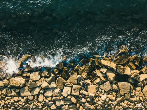 Sahildeki kayalara vuran deniz dalgalarının havadan görünüşü.