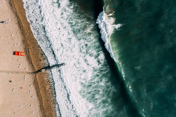 Rif van een zeegolf. Rode catamaran aan de kust. Een pier voor surfers. — Stockfoto