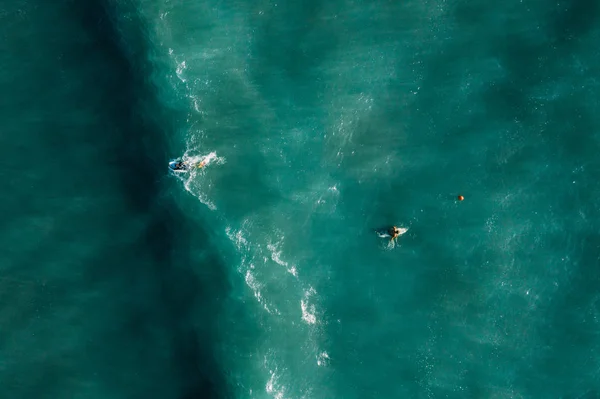 Vista aérea de los surfistas esperando, remando y disfrutando de las olas en un hermoso agua azul — Foto de Stock