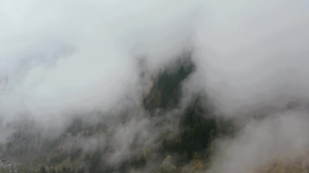Drone vole à travers le brouillard d'automne et les nuages au-dessus des montagnes vers le village et le fjord . — Video