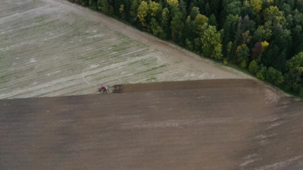 4k aerial drone shot of red tractor cultivating field in country during autumn. — Stockvideo