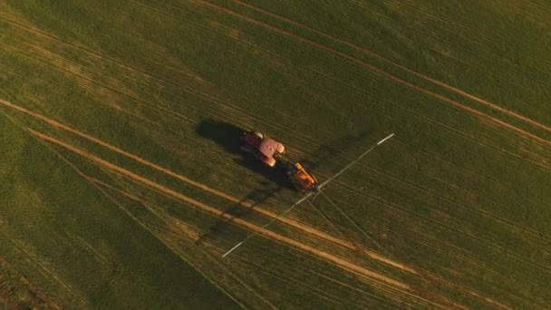 Luchtfoto van landbouwtrekkers die bij zonsondergang op het veld sproeien met sproeiers, herbiciden en pesticiden. Landbouwmachines die insecticide spuiten op het groene veld, agrarische natuurlijke seizoensgebonden lentewerken. — Stockvideo