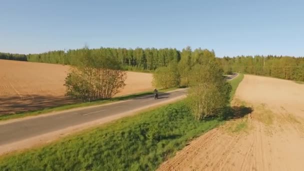 Letecký pohled. Krásný výhled na projíždějící motocykl na venkovské asfaltové silnici. Za jasného letního dne. — Stock video