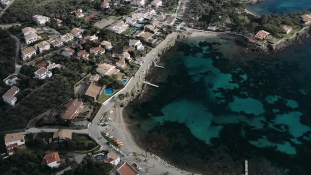 Dritto giù drone vista delle acque turchesi della baia, spiaggia, lungomare e case bianche con tetti piastrellati su di esso, strette strade della città spagnola costiera Cadaques — Video Stock