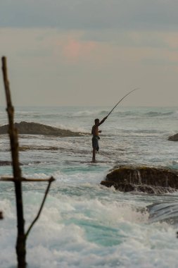 Geleneksel Sri Lankalı balıkçıların siluetleri Koggala, Sri Lanka 'da fırtınalı bir havada. Stilt balıkçılığı, Sri Lanka adasına özgü bir balıkçılık metodudur.