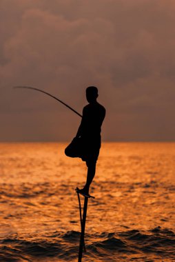 Geleneksel Sri Lankalı balıkçıların siluetleri Koggala, Sri Lanka 'da fırtınalı bir havada. Stilt balıkçılığı, Sri Lanka adasına özgü bir balıkçılık metodudur.