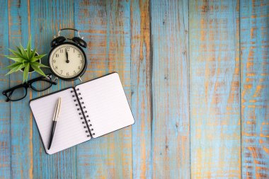 Minimalist düz konum kitap, dolmakalem, bitki, antika saat ve gözlük ahşap masa üst görünümü