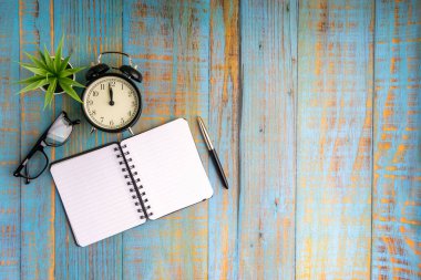 Minimalist düz konum kitap, dolmakalem, bitki, antika saat ve gözlük ahşap masa üst görünümü