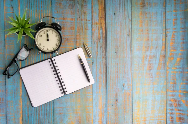 Minimalist flat lay composition of book, fountain pen, plant, vintage clock and glasses on the wooden table top view