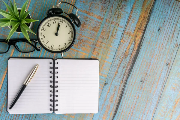 Minimalist flat lay composition of book, fountain pen, plant, vintage clock and glasses on the wooden table top view