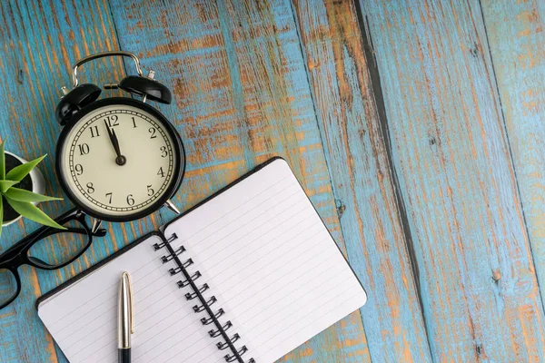 Minimalist flat lay composition of book, fountain pen, plant, vintage clock and glasses on the wooden table top view