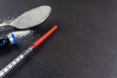 Minimalist düz kompozisyon şeker, kaşık, şırınga ve şişeler koyu arkaplanda. Tıbbi, Sağlık ve Diyabet Konsepti. Üst görünüm ve seçici odak.