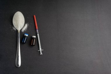 Minimalist düz kompozisyon şeker, kaşık, şırınga ve şişeler koyu arkaplanda. Tıbbi, Sağlık ve Diyabet Konsepti. Üst görünüm ve seçici odak.