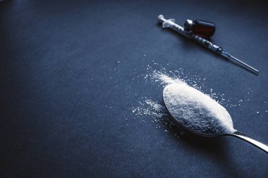 Minimalist düz kompozisyon şeker, kaşık, şırınga ve şişeler koyu arkaplanda. Tıbbi, Sağlık ve Diyabet Konsepti. Üst görünüm ve seçici odak.