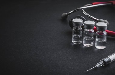 Stetoskop, şişeler ve siyah arka planda şırınga. Seçici odak ve kopyalama alanı