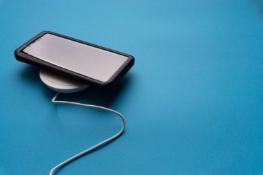 Akıllı telefon şarj oluyor mavi arka planda ya da rıhtımda. Kablosuz şarj ve kopyalama alanı 