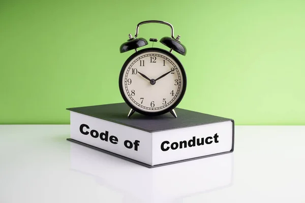 CODE OF CONDUCT text, Alarm Clock and book on green background. Copy space, business and legal concept
