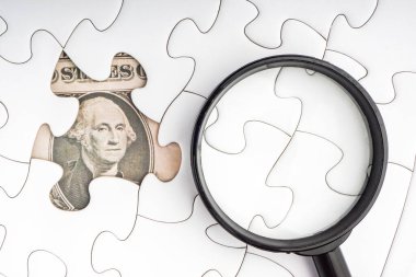 Biz dolar banknotları ve beyaz yapboz üzerinde büyüteç. İş ve kopyalama alanı kavramı