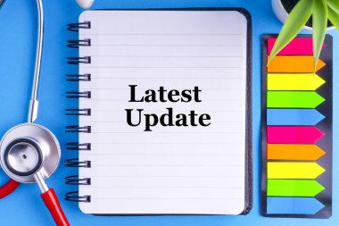 Steteskop, kitap, vazo ve mavi arkaplan üzerine yapışkan notlar içeren son UPdate metni. Sağlık ve iş konsepti