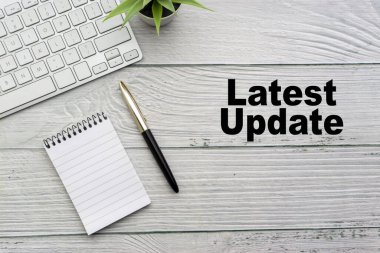 Not defteri, klavye, dekoratif vazo ve ahşap zemin üzerinde dolmakalem olan LATEST UPDATE metin. İş ve kopyalama alanı kavramı