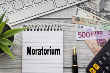 Not defteri, klavye, dekoratif vazo, dolmakalem, hesap makinesi ve tahtadan arkaplandaki para birimiyle MoratORIUM metni. İş ve Kopyalama alanı kavramı