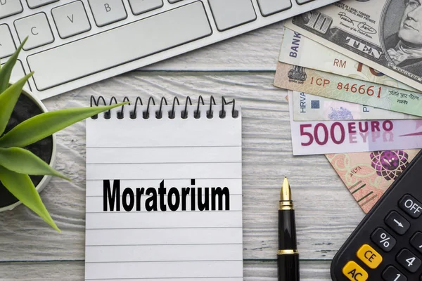 Not defteri, klavye, dekoratif vazo, dolmakalem, hesap makinesi ve tahtadan arkaplandaki para birimiyle MoratORIUM metni. İş ve Kopyalama alanı kavramı