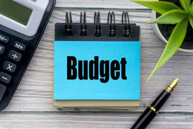 Dekoratif çiçekli bütçe metni, dolma kalem, hesap makinesi ve ahşap arka planda not defteri. İş konsepti