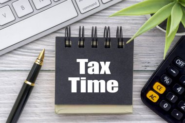 Dekoratif çiçek, hesap makinesi, dolmakalem, klavye ve tahta zemin üzerinde not defteri olan Vergi Time metni. İş ve iletişim kavramı