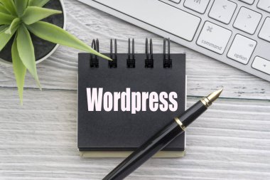 Dekoratif çiçek, klavye, not defteri ve tahta arka planda dolmakalem içeren Wordpress metni. İş ve teknoloji kavramı