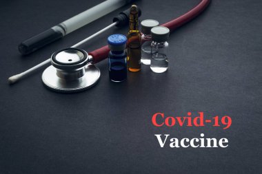 COVID-19 ya da CORONAVIRUS VACCINE metin steteskop, tıbbi çubuk ve şişe siyah arka planda. Covid-19 veya Coronavirus konsepti. 