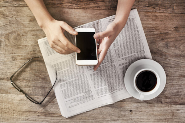 Young woman reading newspaper and holding phone