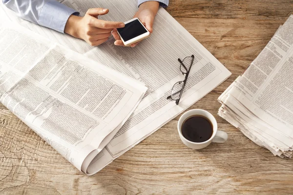 Mujer joven leyendo el periódico y sosteniendo el teléfono —  Fotos de Stock