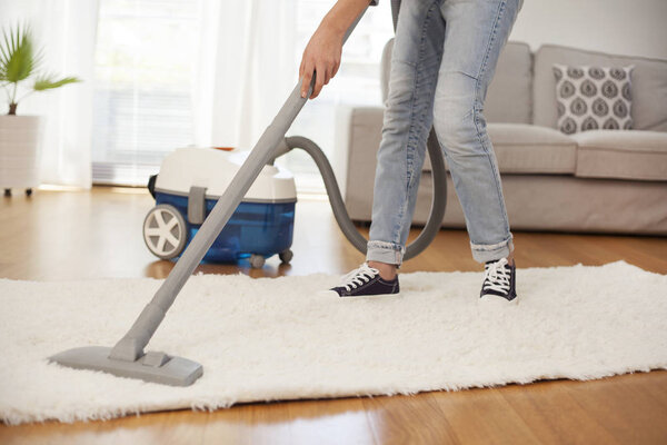Woman cleaning carpet with a vacuum cleaner in room