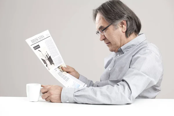 Hombre mayor leyendo periódico sobre fondo gris — Foto de Stock