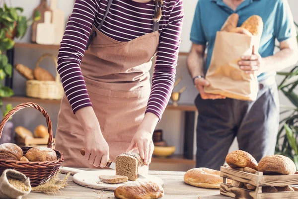 Mãos femininas cortando pão de trigo integral — Fotografia de Stock