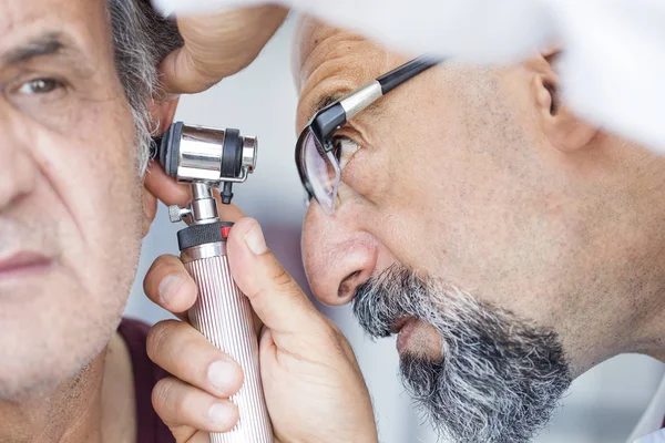 Arzt hält Otoskop in der Hand und untersucht Ohr des Seniors — Stockfoto