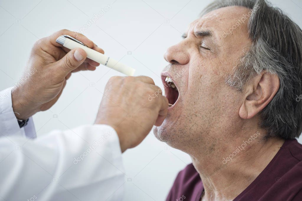 Doctor examines senior man for sore throat