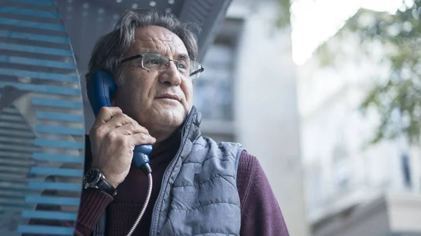 Старший чоловік розмовляє на громадському телефоні на відкритому повітрі — стокове фото