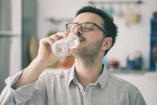 Joven bebiendo agua de la botella en la cocina — Foto de Stock