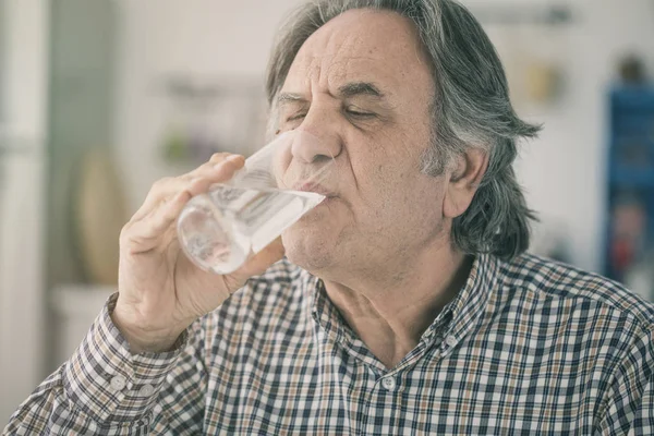 Senior man drinking water from glass in kitchen — Stock Photo, Image