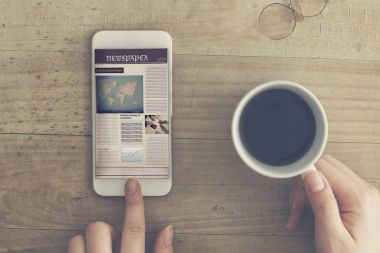 Kahve fincanı tutan cep telefonundan gazete okuma