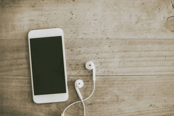 Telefone celular branco e fone de ouvido em fundo de madeira — Fotografia de Stock
