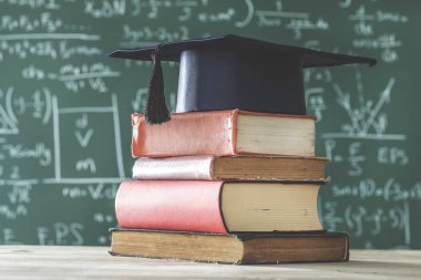 Yığın kitap lisansüstü şapka önünde yeşil yazı tahtası