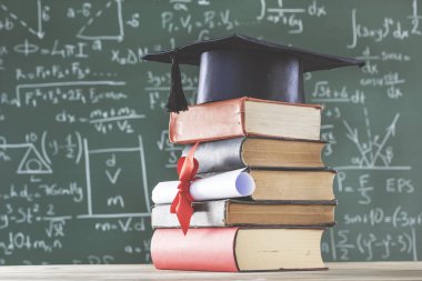 Yığın kitap lisansüstü şapka ve diploma yeşil kara tahta önünde