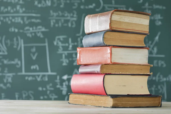 Stack books in front of  green chalkboard