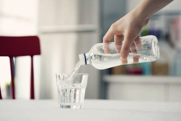 Mano vertiendo agua de la botella al vidrio en la cocina — Foto de Stock