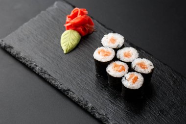 Siyah arka planda somon balıklı Maki Suşi Rolls. Zencefil ve wasabi ile. Suşi menüsü. Japon yemeği. Sushi dürümlü lezzetli Japon yemeklerini yakından çek. Yatay fotoğraf