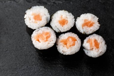 Siyah arka planda somon balıklı Maki Suşi Rolls. Suşi menüsü. Japon yemeği. Sushi dürümlü lezzetli Japon yemeklerini yakından çek. Yatay fotoğraf
